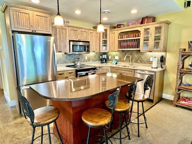 kitchen featuring a breakfast bar area, light brown cabinetry, stainless steel appliances, sink, and decorative light fixtures