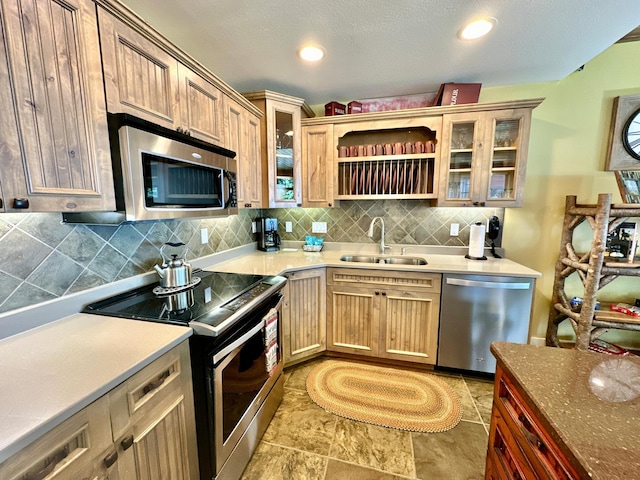 kitchen featuring recessed lighting, glass insert cabinets, a sink, stainless steel appliances, and tasteful backsplash