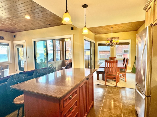 kitchen with freestanding refrigerator, a breakfast bar area, an inviting chandelier, hanging light fixtures, and a kitchen island