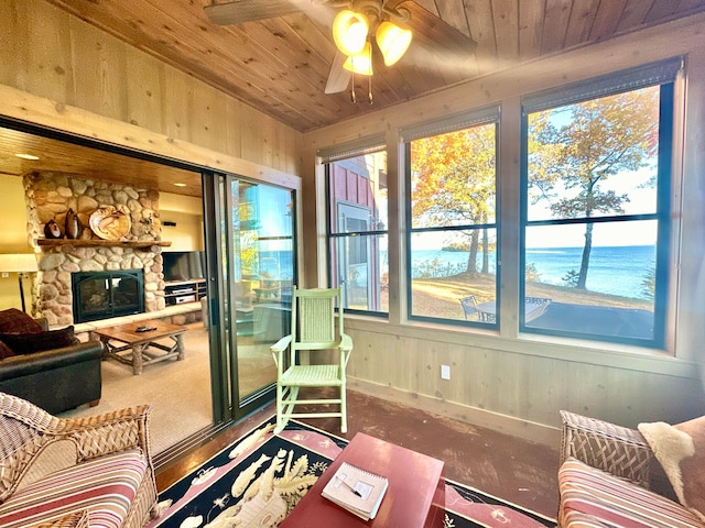 sunroom featuring wooden ceiling, wooden walls, a fireplace, and a ceiling fan