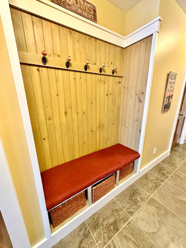 mudroom featuring dark tile patterned flooring and wood walls