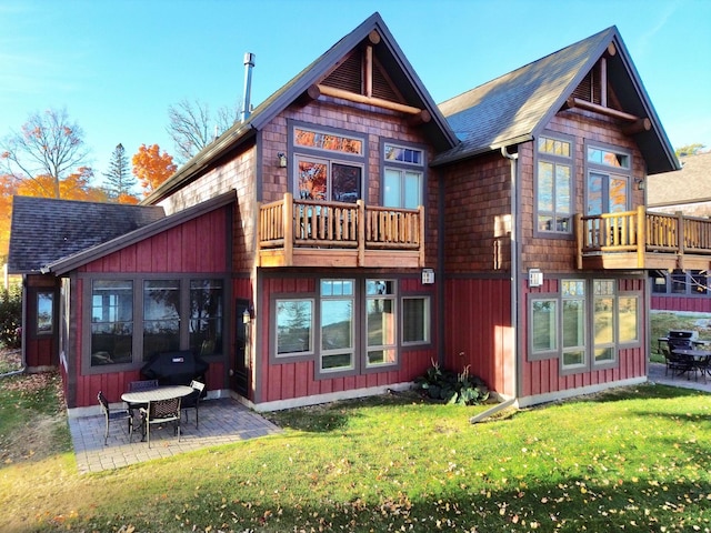 rear view of house featuring a shingled roof, a patio area, and a lawn
