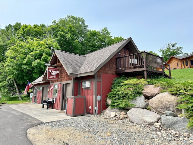 exterior space with a wooden deck, a shingled roof, and an AC wall unit