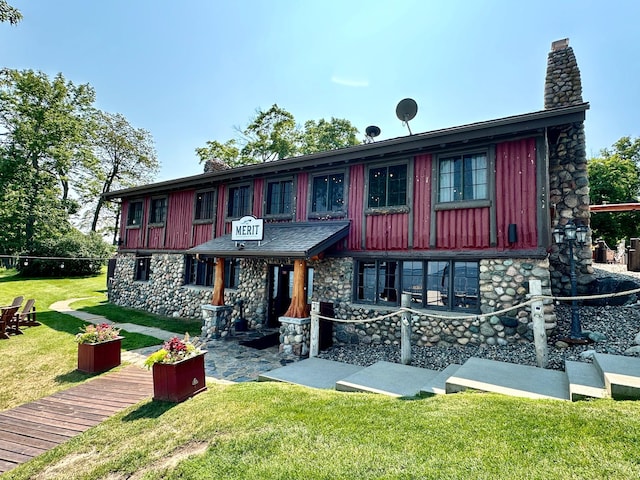 view of front facade with a chimney, a front lawn, stone siding, and board and batten siding