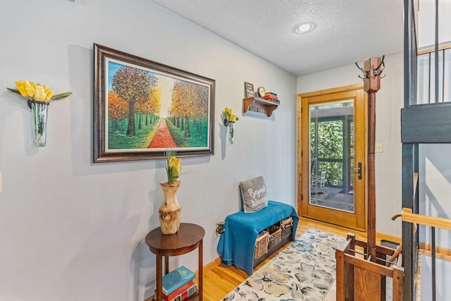 doorway with light wood-style floors, baseboards, and a textured ceiling