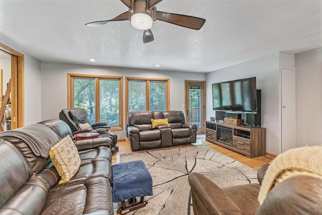 living room with light wood-style flooring, baseboards, ceiling fan, and a textured ceiling