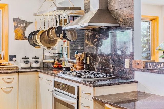 kitchen featuring tasteful backsplash, wall chimney exhaust hood, dark stone countertops, white oven, and stainless steel gas cooktop