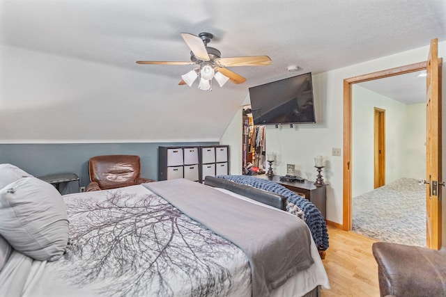 bedroom with a ceiling fan, vaulted ceiling, a textured ceiling, and wood finished floors