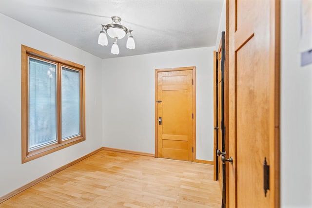 empty room with light wood-type flooring, baseboards, and a textured ceiling