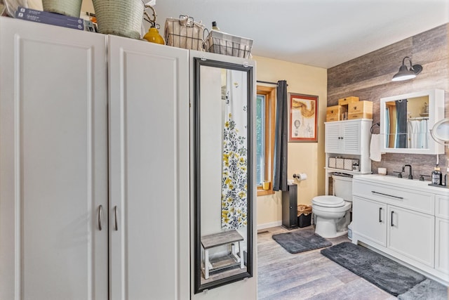 bathroom featuring wooden walls, decorative backsplash, toilet, wood finished floors, and vanity