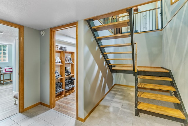 stairway featuring a textured ceiling, tile patterned floors, and baseboards