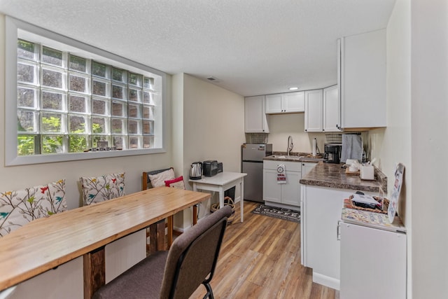 kitchen featuring white cabinets, dark countertops, light wood-style flooring, freestanding refrigerator, and a sink