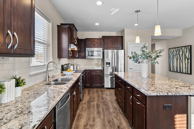 kitchen with dark wood-style floors, stainless steel appliances, a kitchen island, a sink, and dark brown cabinetry