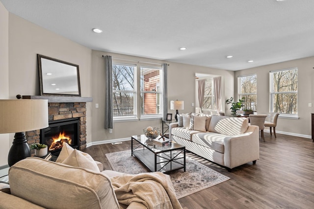 living area featuring dark wood finished floors, plenty of natural light, a stone fireplace, and baseboards