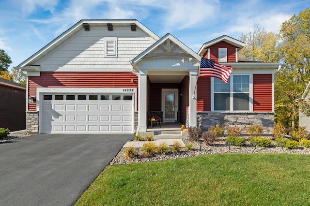 view of front of home featuring an attached garage, stone siding, aphalt driveway, and a front yard