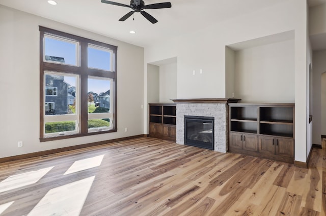 unfurnished living room with ceiling fan, a stone fireplace, and light wood-type flooring