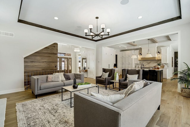 living room with visible vents, crown molding, light wood-style flooring, and an inviting chandelier