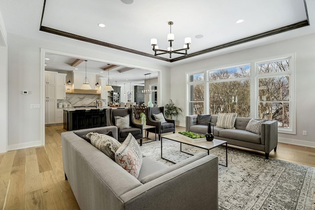 living area with baseboards, a raised ceiling, light wood-style flooring, a notable chandelier, and recessed lighting