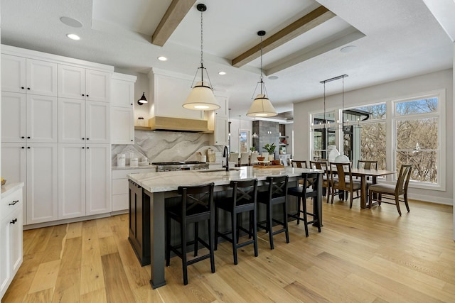 kitchen with light wood finished floors, decorative backsplash, beam ceiling, and white cabinets