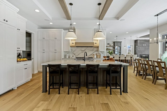 kitchen featuring light wood-style flooring, white cabinetry, decorative backsplash, and beam ceiling