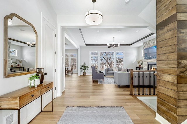 entryway featuring light wood finished floors, a raised ceiling, a notable chandelier, and a glass covered fireplace