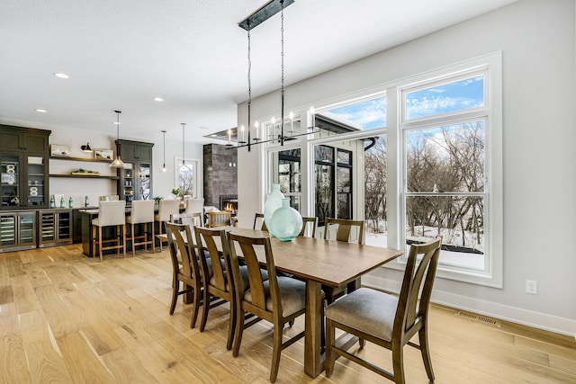 dining space with light wood-style floors, a large fireplace, visible vents, and baseboards