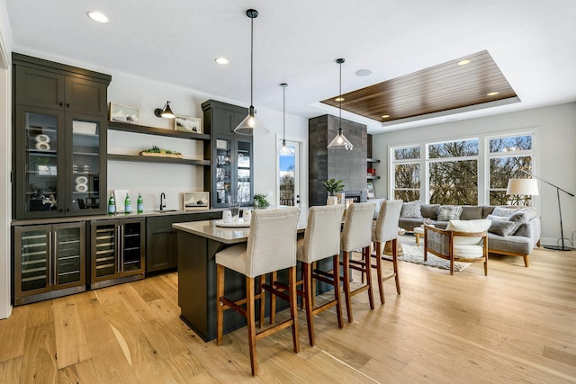 bar featuring beverage cooler, a tray ceiling, light wood-type flooring, and wet bar