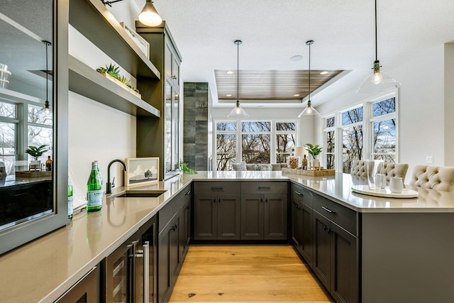 bar featuring light wood-style floors, beverage cooler, pendant lighting, and a sink