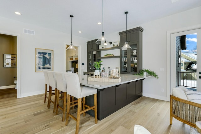 bar featuring light wood-type flooring, baseboards, visible vents, and decorative light fixtures