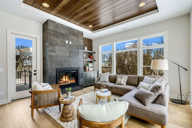 living room with wooden ceiling, light wood-style flooring, a raised ceiling, and a tiled fireplace