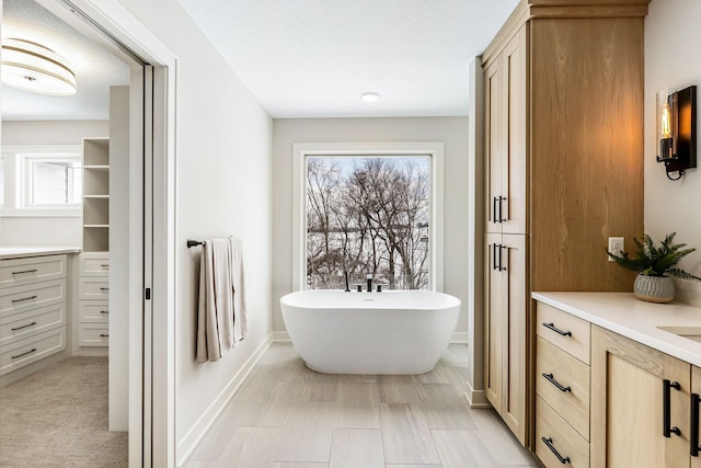 full bath with a closet, a freestanding bath, vanity, and baseboards