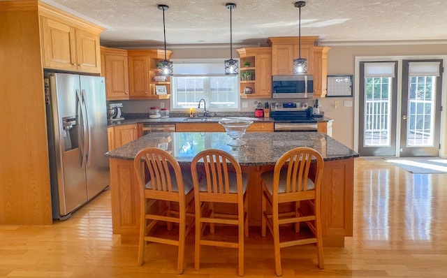 kitchen with appliances with stainless steel finishes, a kitchen island, a textured ceiling, and a healthy amount of sunlight