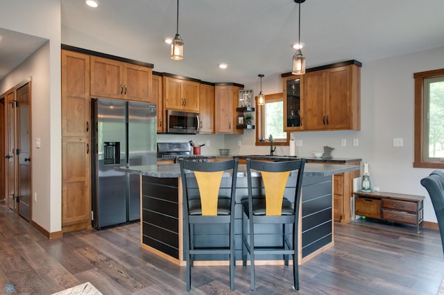 kitchen with hanging light fixtures, dark hardwood / wood-style floors, a kitchen island, a breakfast bar area, and stainless steel appliances