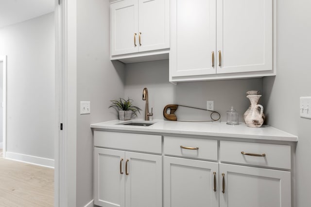 interior space with white cabinetry, sink, light stone countertops, and light wood-type flooring