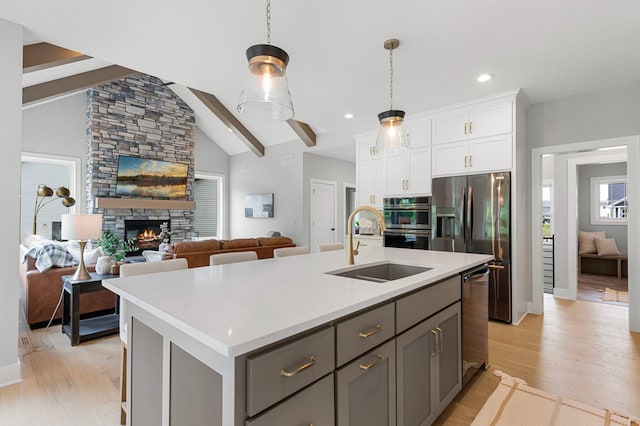 kitchen featuring gray cabinetry, an island with sink, white cabinets, beamed ceiling, and light wood-type flooring