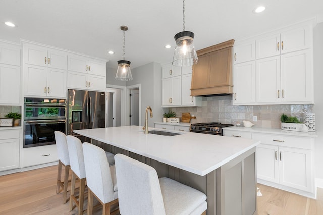 kitchen featuring an island with sink, sink, custom exhaust hood, and white cabinets