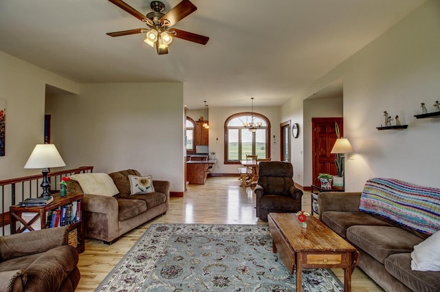 living area with ceiling fan with notable chandelier, light wood-style flooring, and baseboards