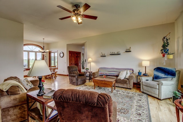 living area featuring ceiling fan with notable chandelier, light wood-type flooring, and baseboards