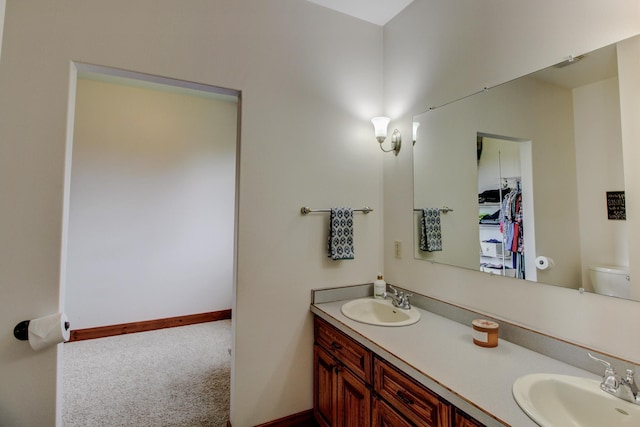 bathroom featuring baseboards, a sink, toilet, and double vanity