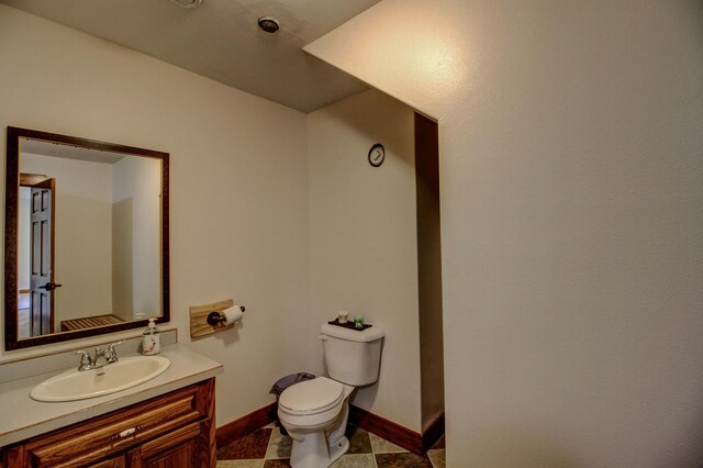 half bathroom featuring toilet, baseboards, and vanity