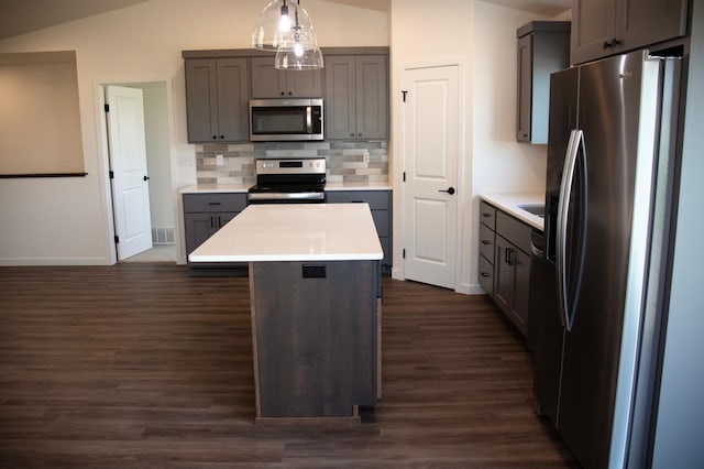 kitchen with appliances with stainless steel finishes, vaulted ceiling, dark hardwood / wood-style floors, pendant lighting, and a center island