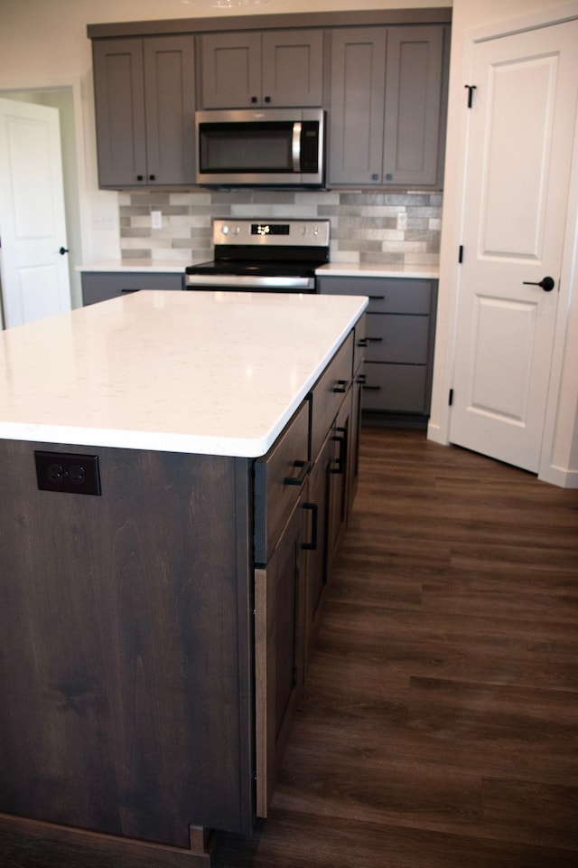 kitchen featuring a kitchen island, dark wood-type flooring, appliances with stainless steel finishes, and backsplash