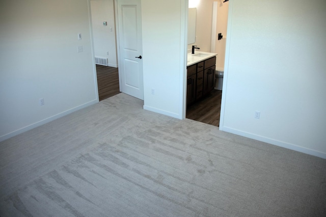 unfurnished bedroom with connected bathroom, sink, and light colored carpet