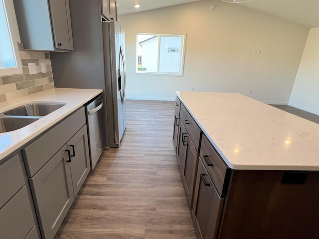 kitchen with lofted ceiling, decorative backsplash, a kitchen island, appliances with stainless steel finishes, and light wood-type flooring