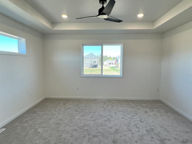 unfurnished room with ceiling fan, a raised ceiling, a wealth of natural light, and light carpet