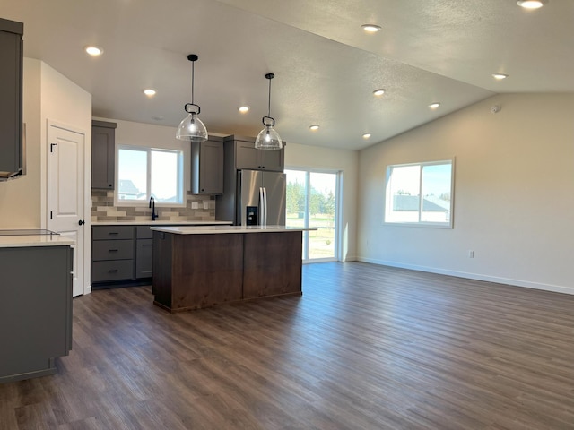 kitchen with dark hardwood / wood-style floors, stainless steel refrigerator with ice dispenser, a center island, vaulted ceiling, and pendant lighting