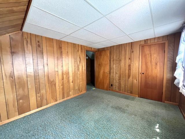 carpeted empty room with wood walls and a drop ceiling