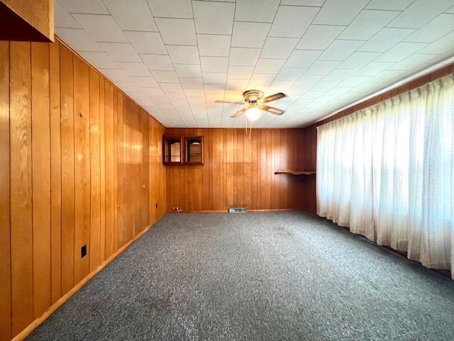 unfurnished room featuring carpet flooring, ceiling fan, and wooden walls