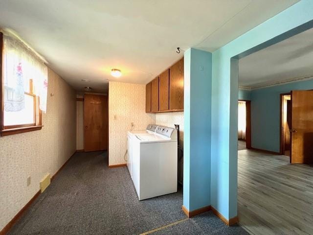 clothes washing area with washing machine and clothes dryer, cabinets, wood-type flooring, and a healthy amount of sunlight