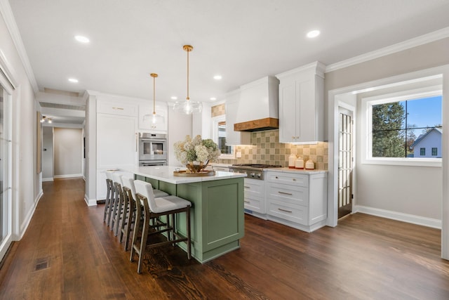 kitchen featuring appliances with stainless steel finishes, white cabinetry, custom range hood, a kitchen island, and a breakfast bar